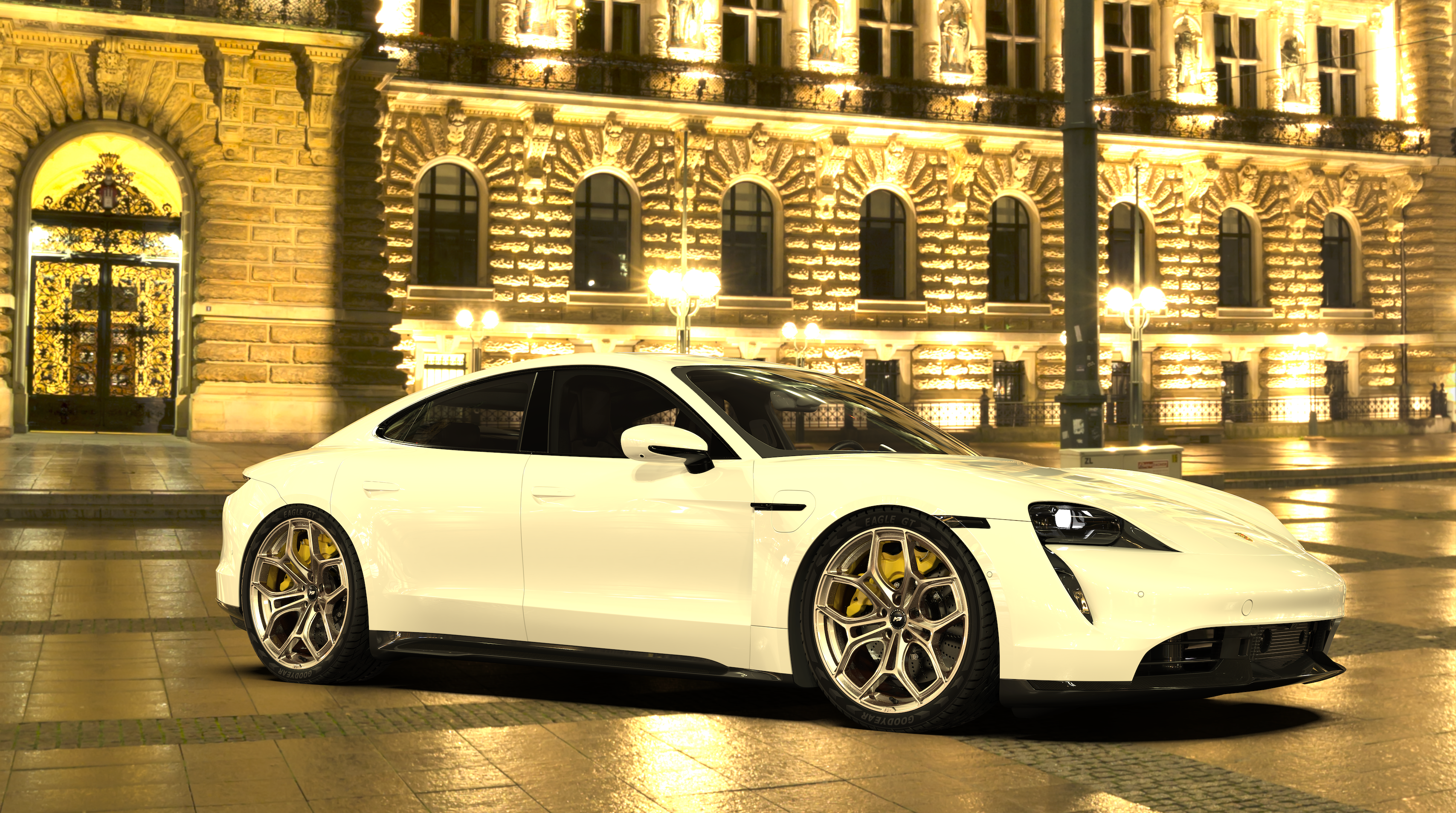 White Porsche Taycan parked at night in front of an illuminated historic building, featuring black forged rims with yellow brake calipers.